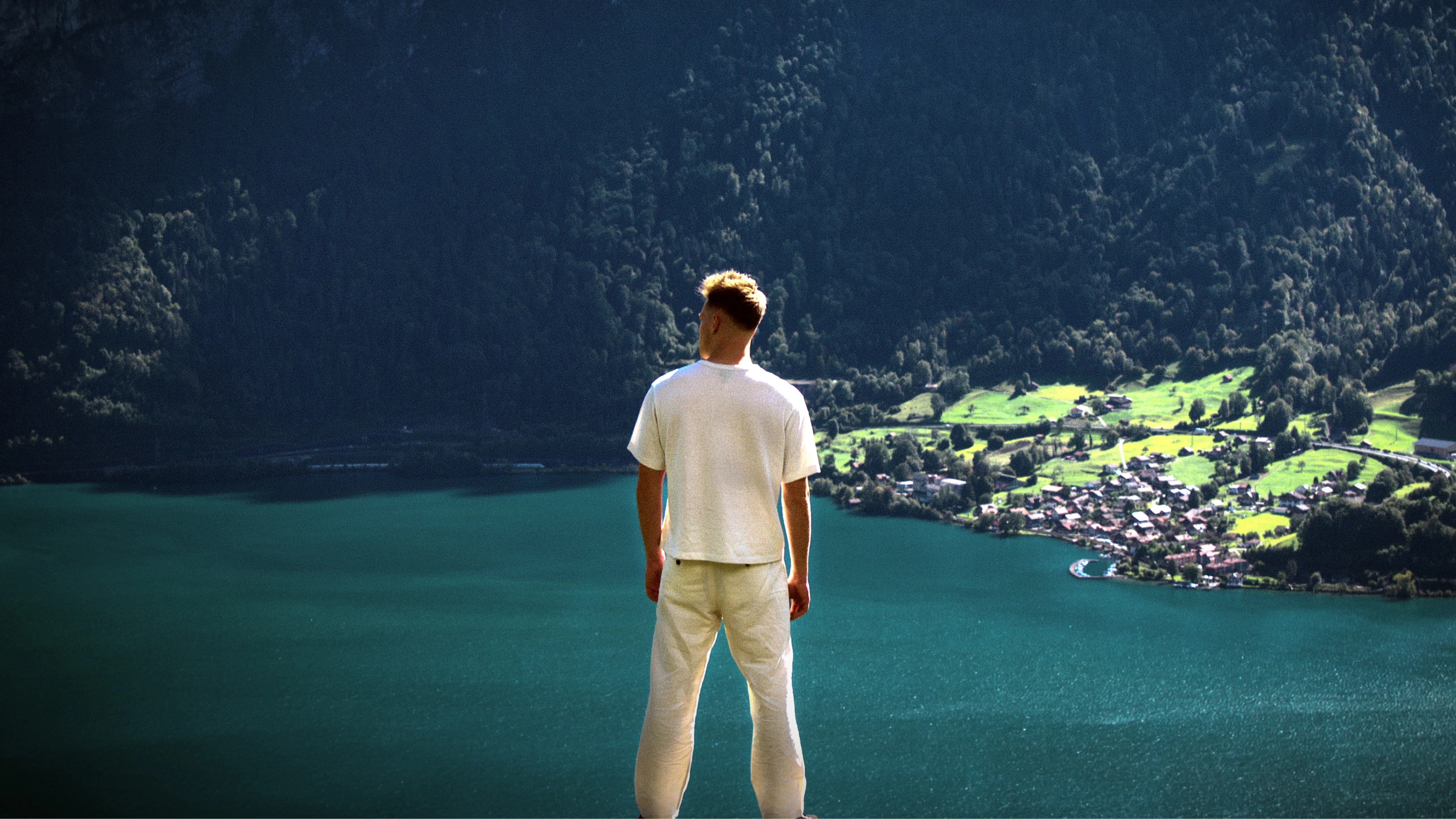 Lukas Goss on a ledge above an alpine lake and village